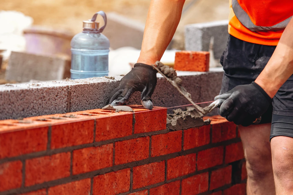 Travailleur qualifié de maçonnerie posant des briques dans un projet de construction sous la lumière du soleil sur un chantier de construction