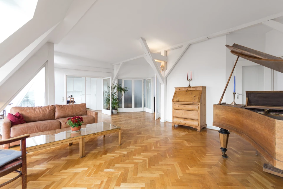 Salon spacieux sous combles avec poutres apparentes blanches, parquet chevrons en bois naturel