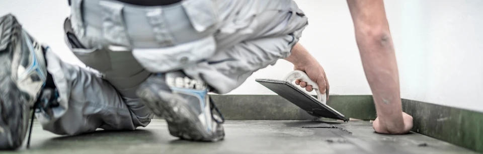 Une personne nettoie un mur carrelé en marbre blanc avec une raclette professionnelle bleue et blanche