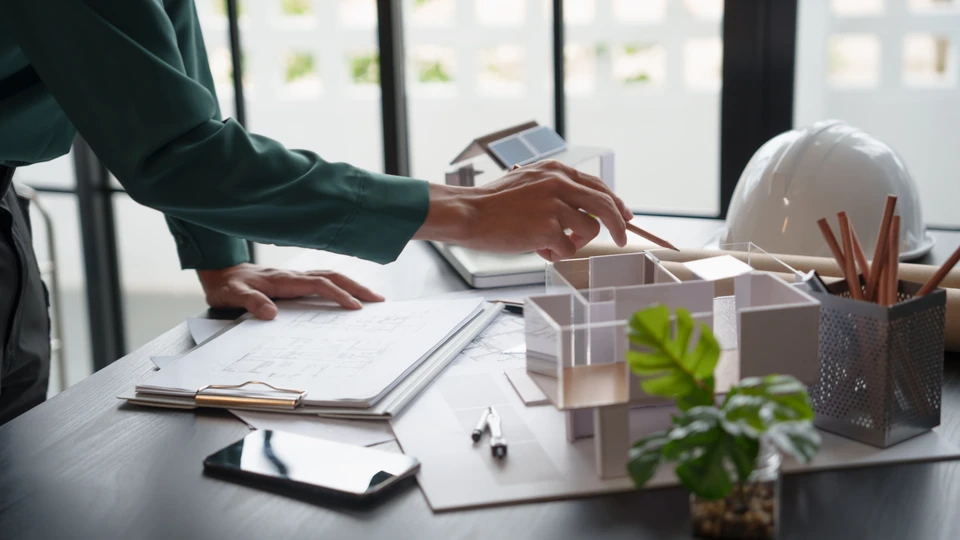 Homme souriant en pull rayé tenant une calculatrice devant un ordinateur portable dans un espace de travail organisé